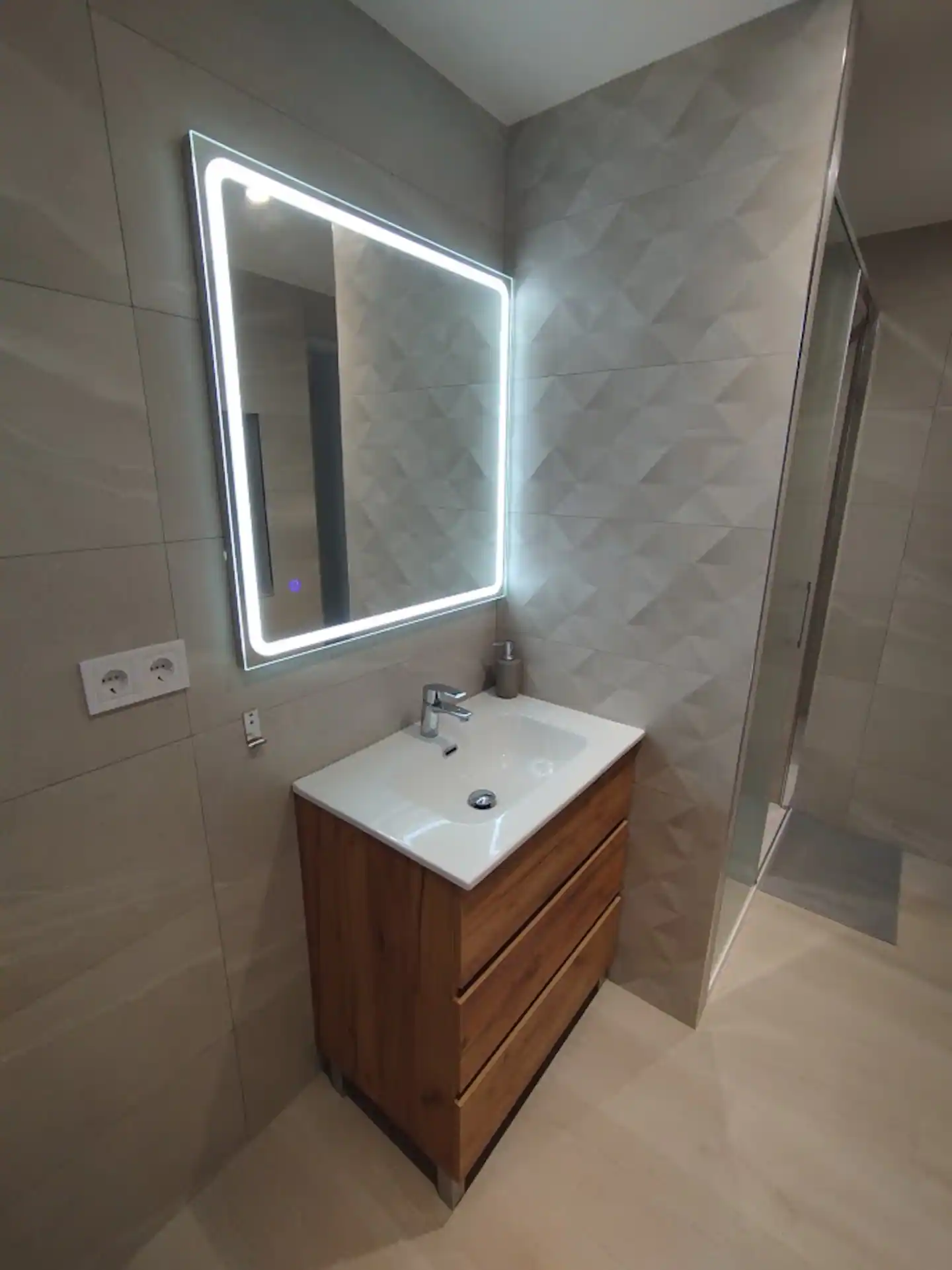 Baño con mueble de madera, espejo iluminado y ducha de obra