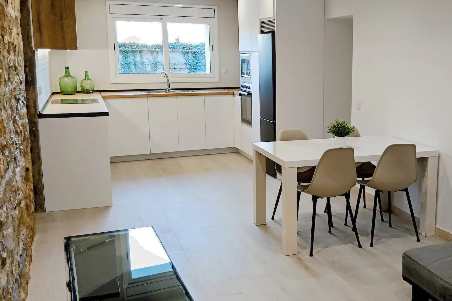 Comedor con mesa y sillas, la cocina blanca al fondo y la cisterna acristalada en el suelo
