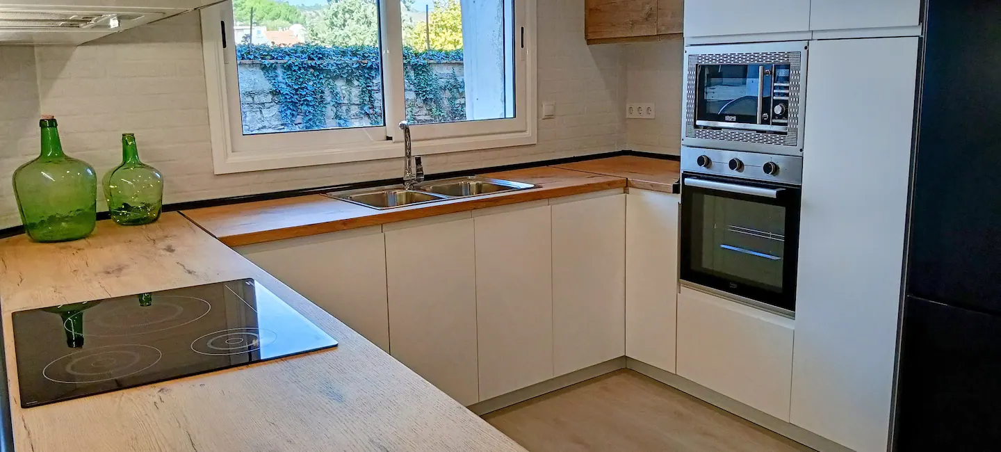 Cocina blanca con encimera de madera, horno, microondas y ventana al patio