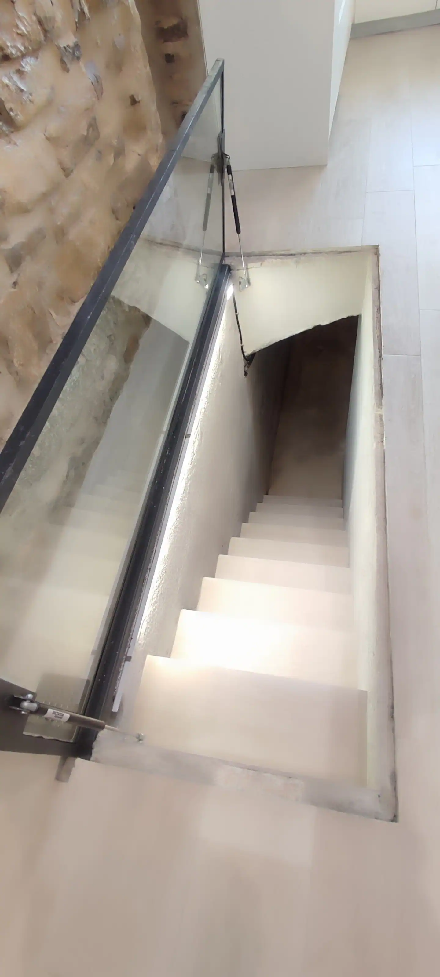 Escalera de piedra que baja a la cisterna, con barandilla de cristal