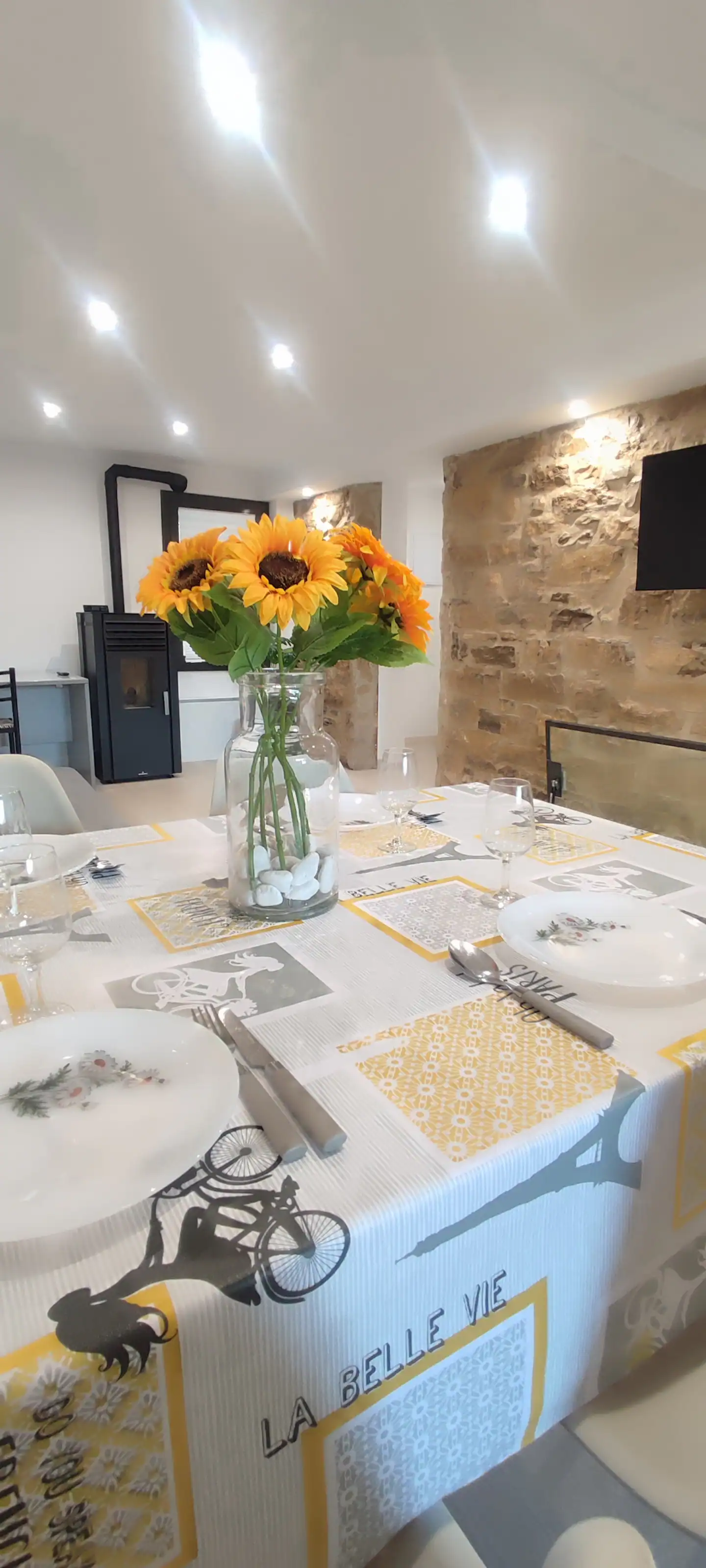 Mesa del comedor puesta, con girasoles y la pared de piedra detrás