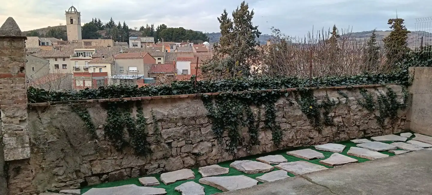 Muro de piedra cubierto de hiedra con los tejados y el campanario del pueblo al fondo